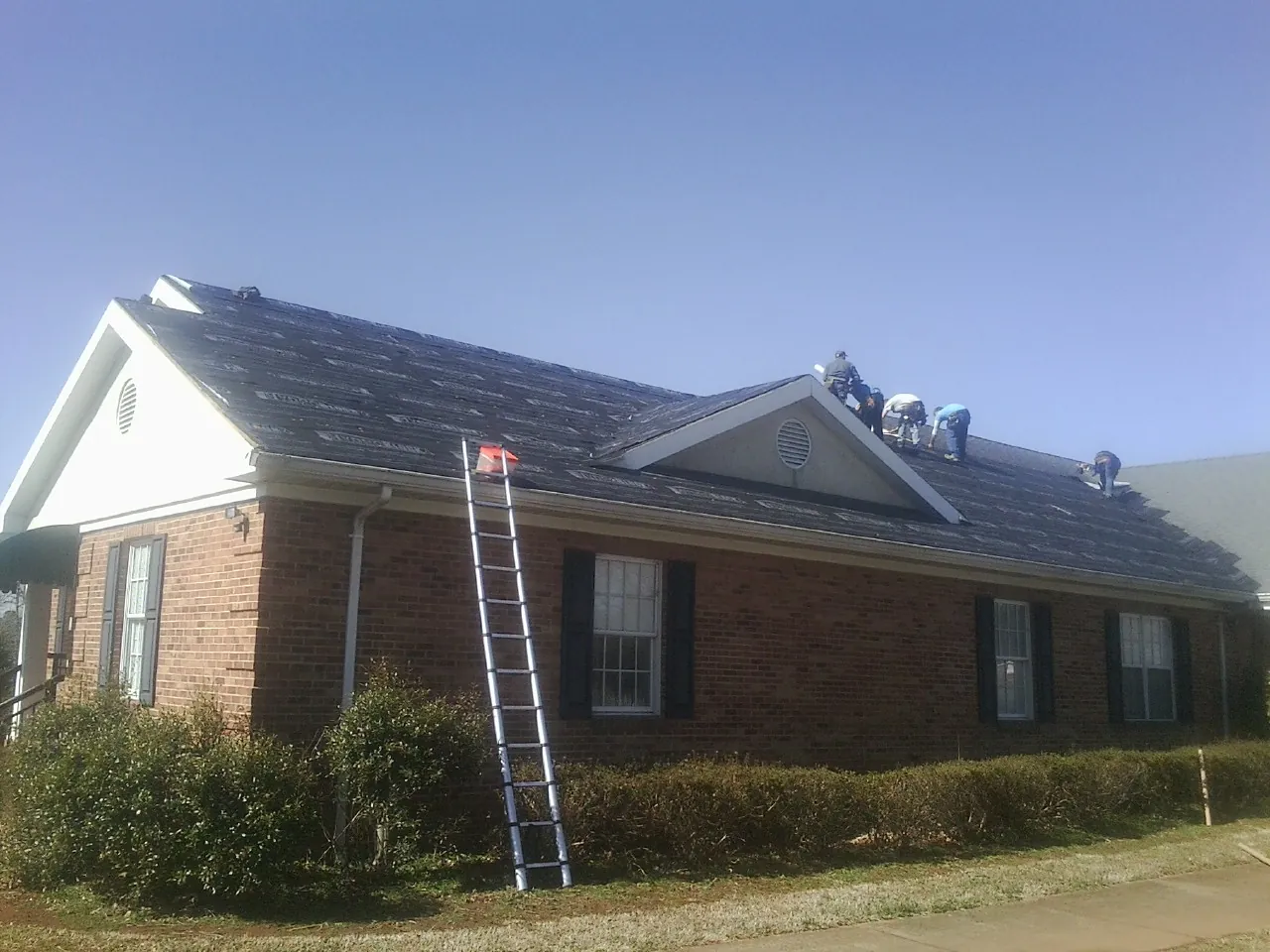 Crew tearing shingles off a brick ranch roof with a ladder set — Metal Roof Repair work by our crew in West Simsbury