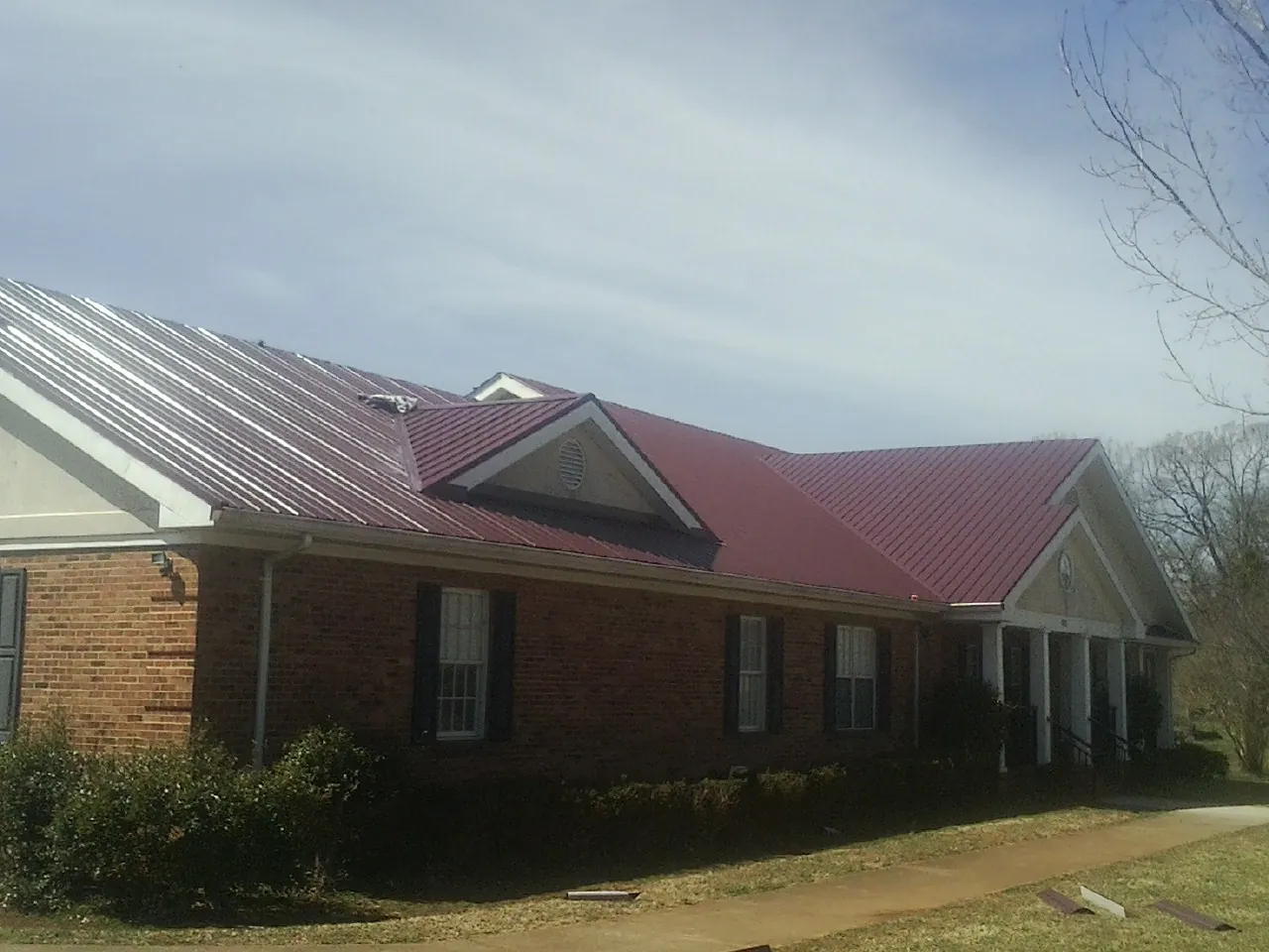 Red metal roof with gabled entries on a long brick building, from a Hail Damage Roof Repair job in West Simsbury