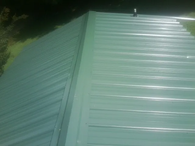New green metal panels meeting at the ridge of a roof — Flat Roof Repair work by our crew in West Simsbury