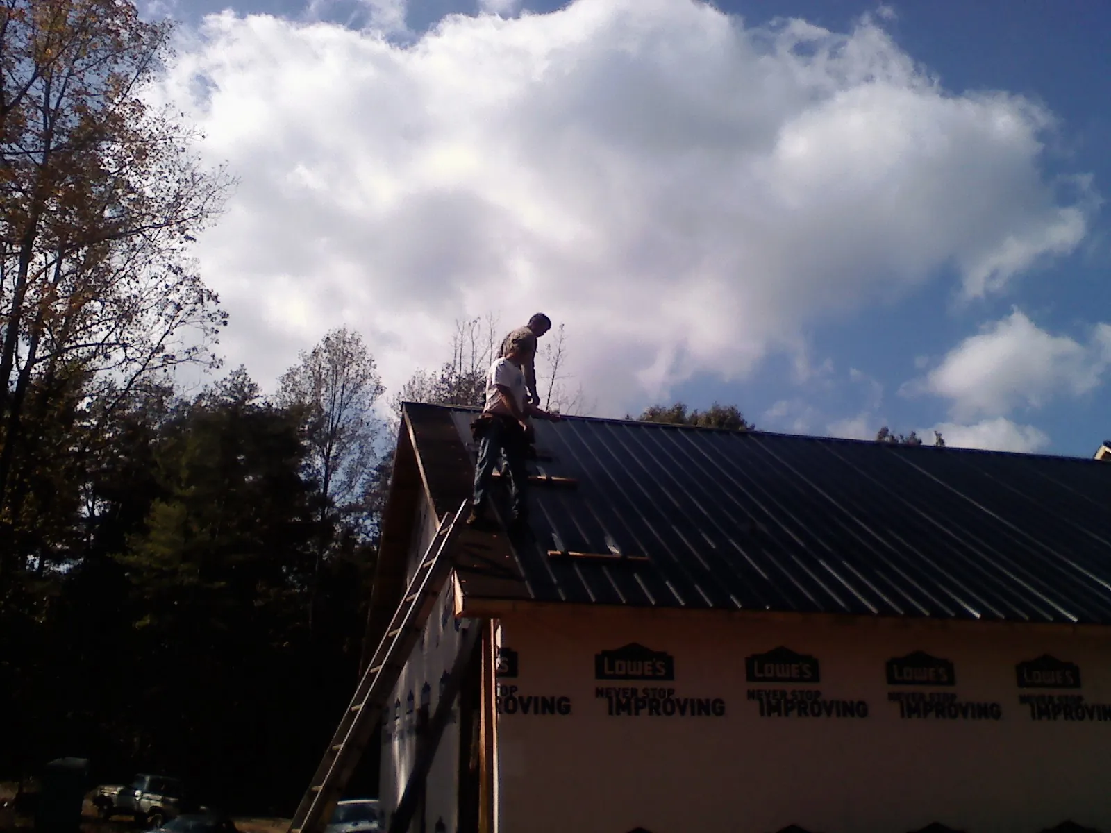 Roofer fastening dark metal panels high against a cloudy sky, from a Roof Inspection job in West Simsbury