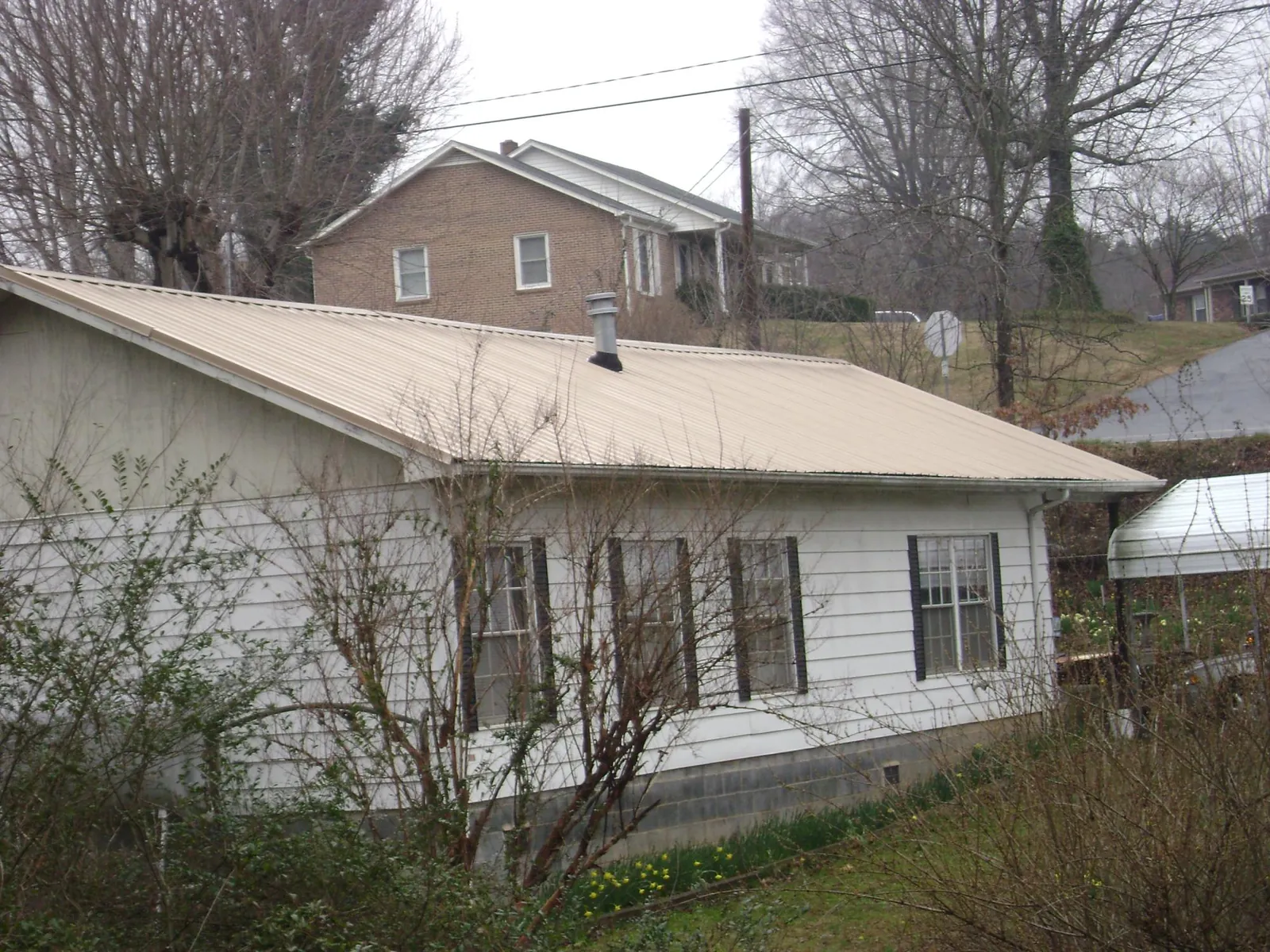 Tan metal roof on a white sided house set into a hillside — Commercial Roofing by Roofing Brothers in West Simsbury